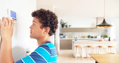 A young boy curiously examines a wall-mounted thermostat in a home setting.