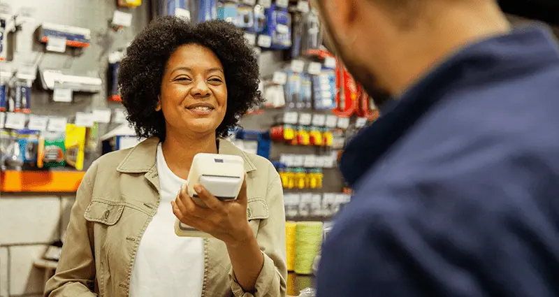 A woman stands in front of a man, holding a cell phone in her right hand, engaged in conversation.