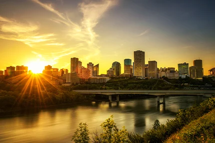 A vibrant sunset casts warm hues over a city skyline, reflecting on a calm river below.