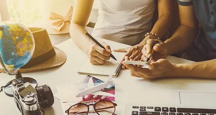 A man and woman sit at a desk, working together with a laptop and a camera in front of them.