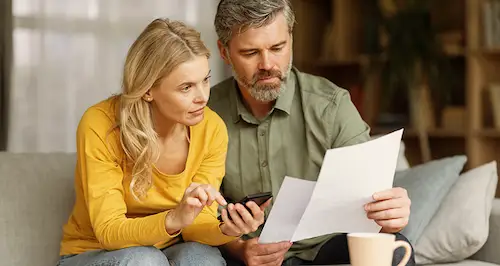 A couple sitting on a couch, reviewing a document together with focused expressions.