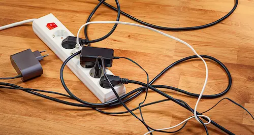 A tangled assortment of wires and cords scattered across a wooden table surface.