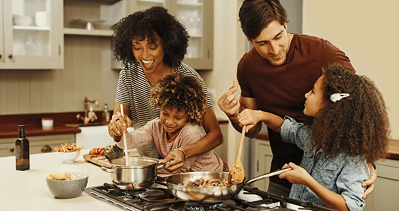 A family of four joyfully cooking together in a bright kitchen, sharing tasks and laughter.