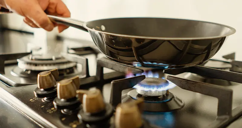 A person is cooking on a stove, using a pan placed on top, focused on preparing a meal.