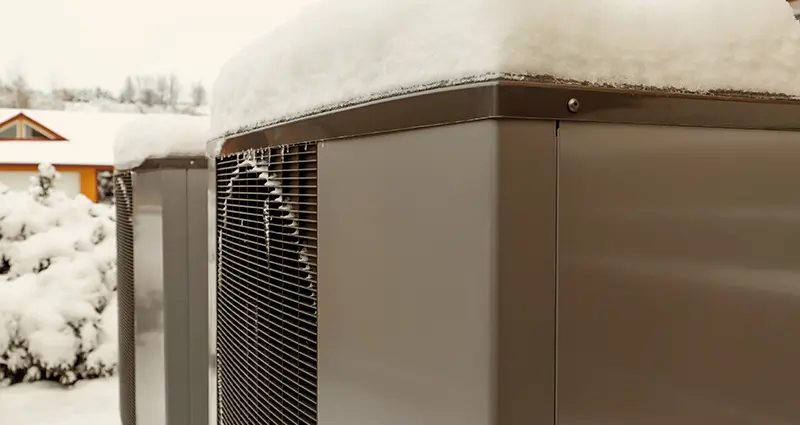 A large air conditioner covered in snow, highlighting winter conditions and its outdoor placement.