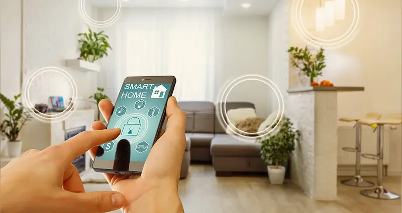 A person holds a smartphone in a cozy living room, surrounded by furniture and decor.