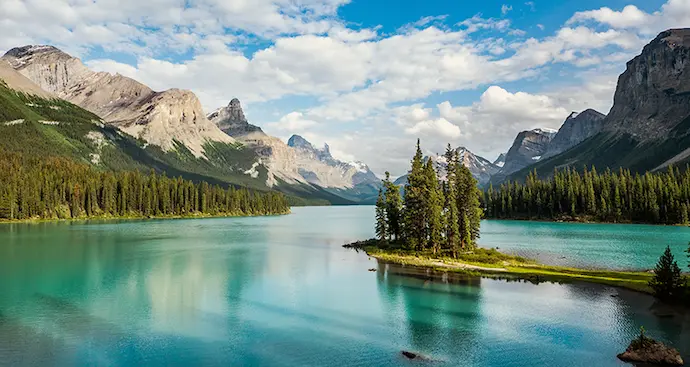 A serene lake nestled among towering mountains and lush green trees under a clear blue sky.
