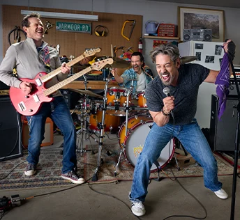 A man in an orange shirt and blue jean shorts skiing down a snowy slope, showcasing his skills by jumping through the air