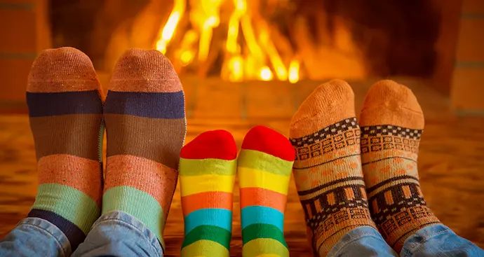 three sets of feet with Christmas socks on sitting in front of a cozy fire. 