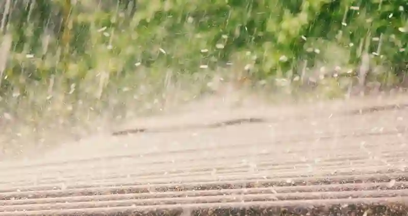 Rainy day scene featuring raindrops falling with a roof visible in the background.