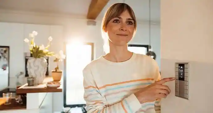 A woman smiling and adjusting a thermostat