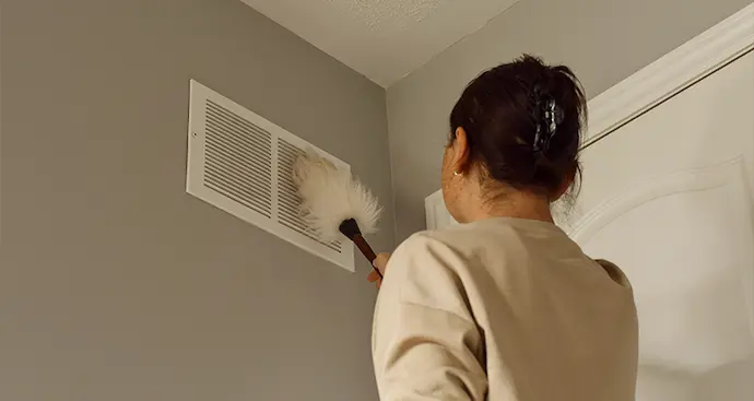 woman cleans vent cover with duster