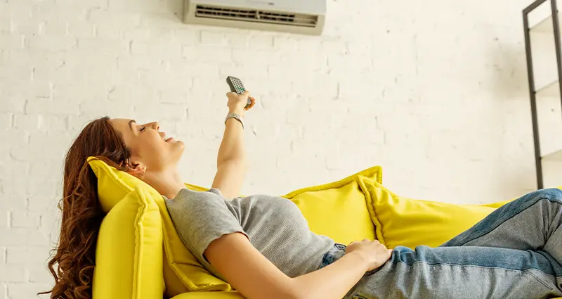 A woman reclines on a couch, holding a remote control in her hand, appearing relaxed and engaged in leisure.