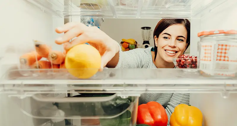 a woman reaching into a refrigerator grabbing a lemon