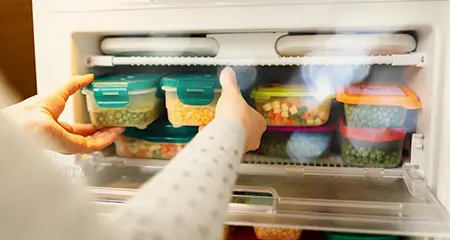 A person reaching into an open refrigerator, looking for food or drinks inside.
