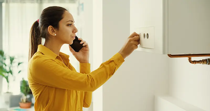 A woman speaks on her cell phone, positioned next to a gas boiler, appearing attentive and engaged in the conversation.