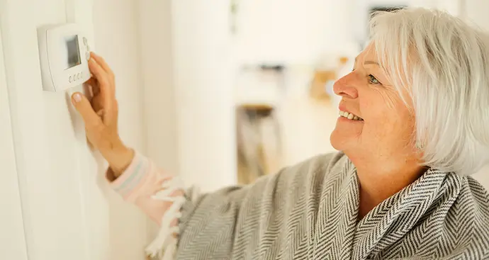 A woman smiles while holding a thermostat, indicating satisfaction with her home's temperature control.