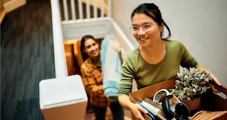 A woman carefully descends stairs while carrying a box filled with various items.