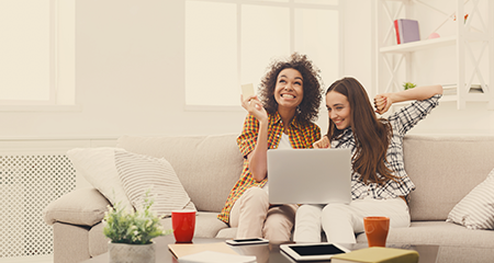Two young women celebrating on couch with laptop on their laps