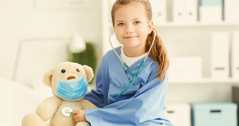 Girl in hospital holding stethoscope to masked teddy bear