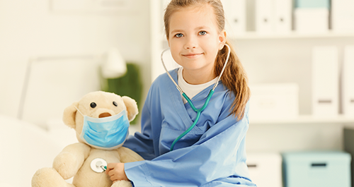 Girl in hospital holding stethoscope to masked teddy bear