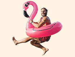 1330613274 Young man jumping in river from deck. He is jumping with pink flamingo swimming float.