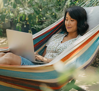 A woman relaxes in a hammock, using a laptop while enjoying a peaceful outdoor setting.