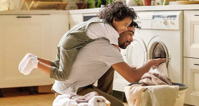 Dad taking laundry out and kid playing on his back