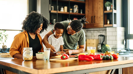 A family collaborates in the kitchen, chopping vegetables and mixing ingredients for a meal preparation.
