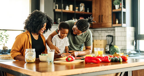 A family collaborates in the kitchen, chopping vegetables and mixing ingredients for a meal preparation.