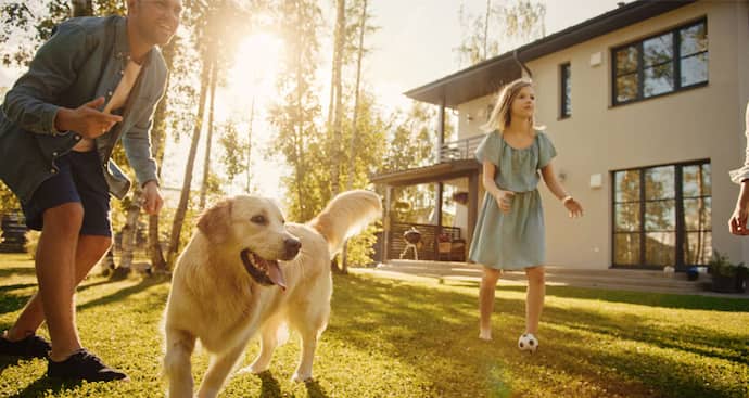 A family is seen walking their dog in backyard of their house, highlighting a cheerful outdoor family activity.