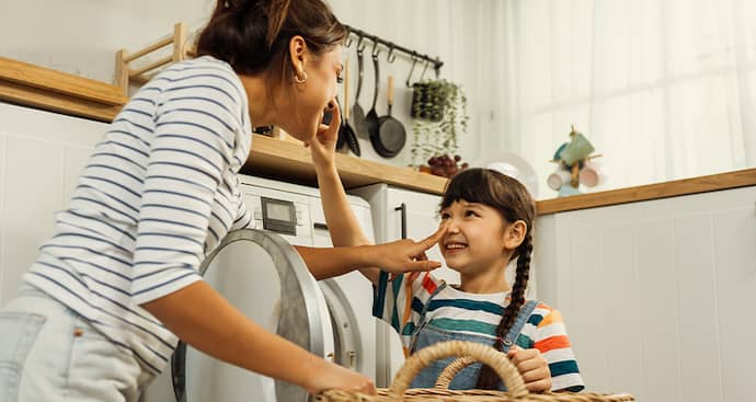 Mother and daughter doing laundry smiling touching each others nose with their finger