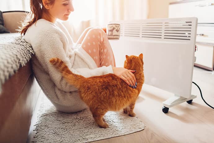 Woman enjoying coffee in front of electric heater with her cat