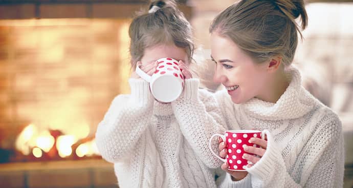 Mother and child drinking hot chocolate on winter evening by fireplace