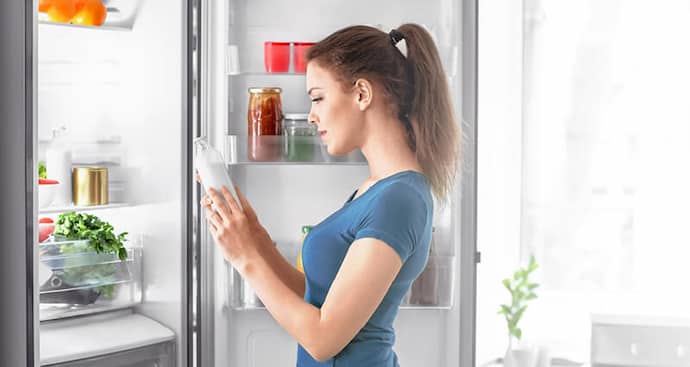Woman holding a bottle standing in front of an open fridge at home