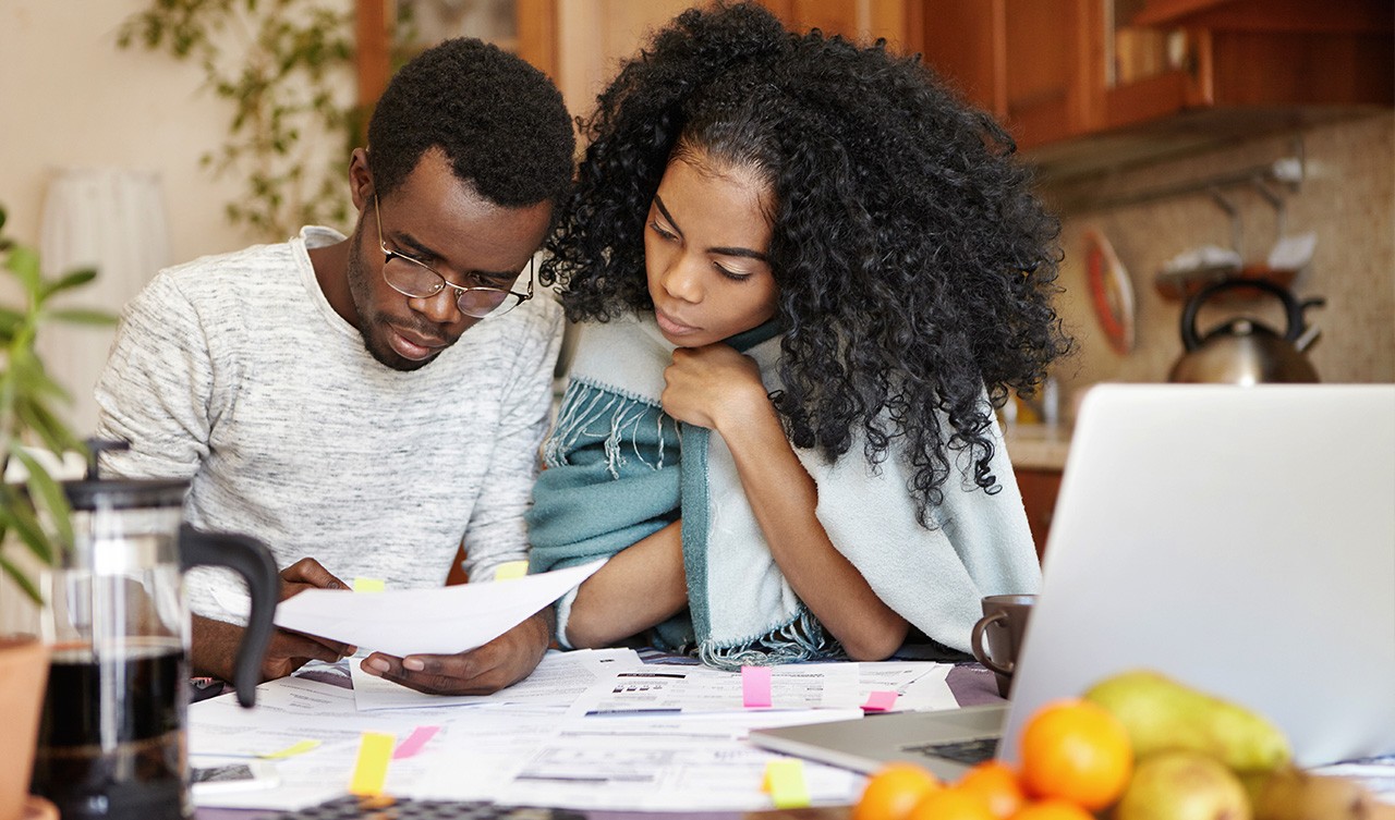 A man and woman sit at a table, focused on a laptop, engaged in discussion or collaboration.