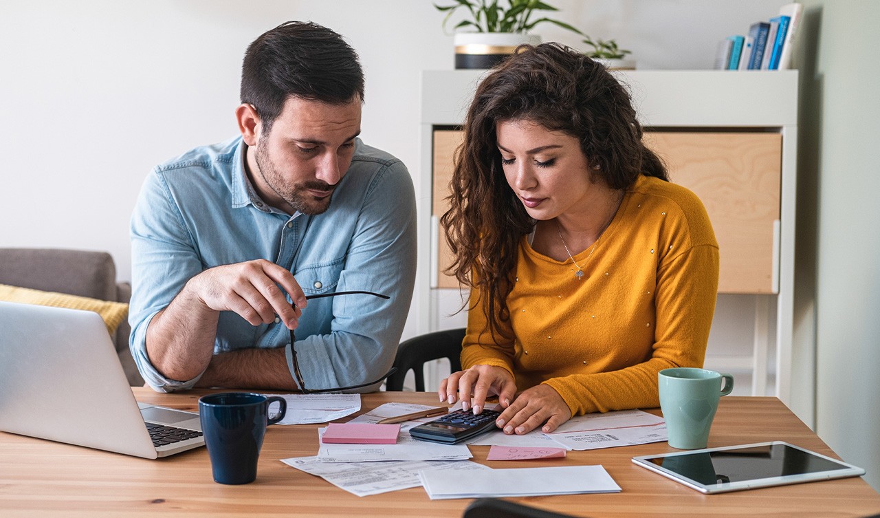 A couple sitting at a table, reviewing financial documents and using a laptop in a cozy home setting.