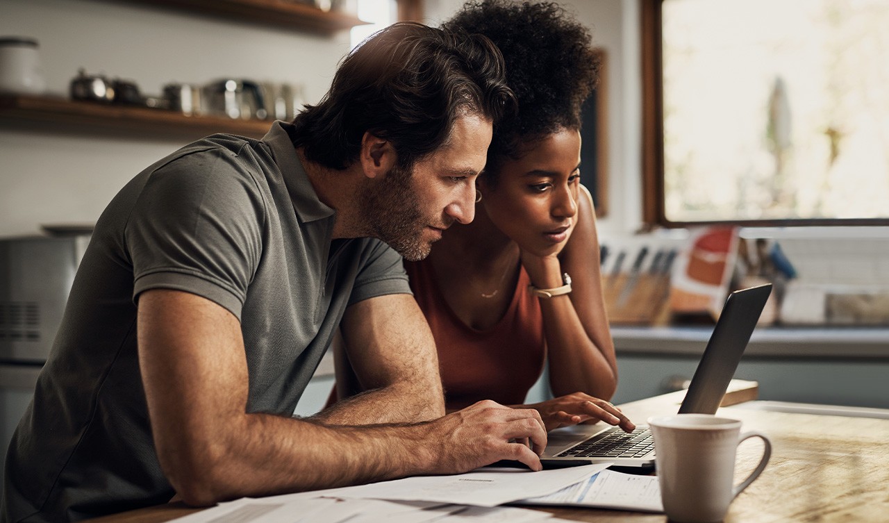 A man and woman are seated together, focused on a laptop screen, discussing its content.