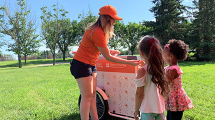 A woman handing treats to two children in a park. 