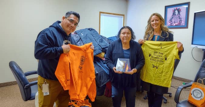 Three people presenting clothing items in an office space.