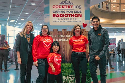 Four people in smiling in front of Country 105 Caring for Kids sign.