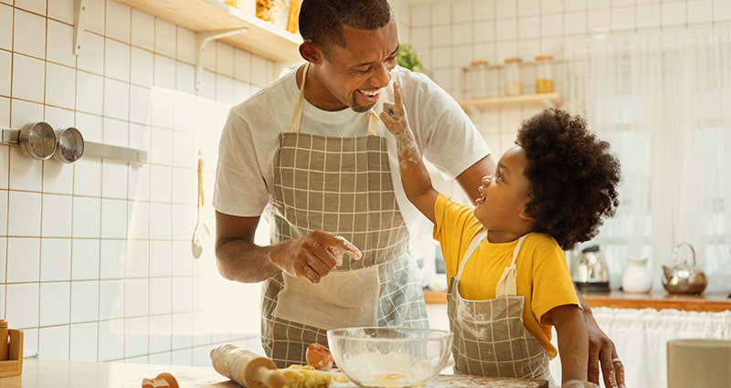 Father and young son baking. Son putting flour on fathers nose.