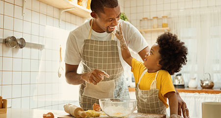 Father and young son baking. Son putting flour on fathers nose.