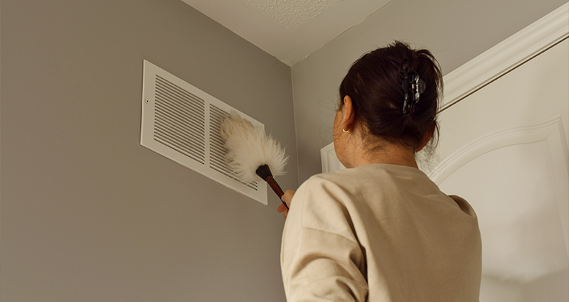 Woman cleaning air vent with duster