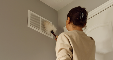 Woman cleaning air vent with duster
