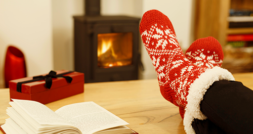Person with festive socks in front of fire with box and book on table