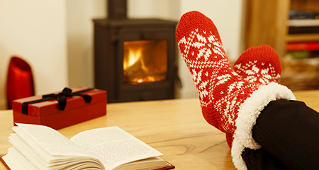 Person with festive socks in front of fire with box and book on table