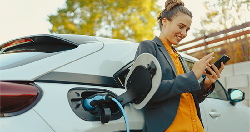 Woman on phone leaning on car while its charging