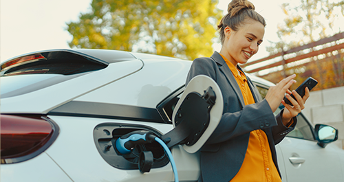 Woman on phone leaning on car while its charging