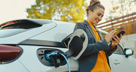 Woman on phone leaning on car while its charging